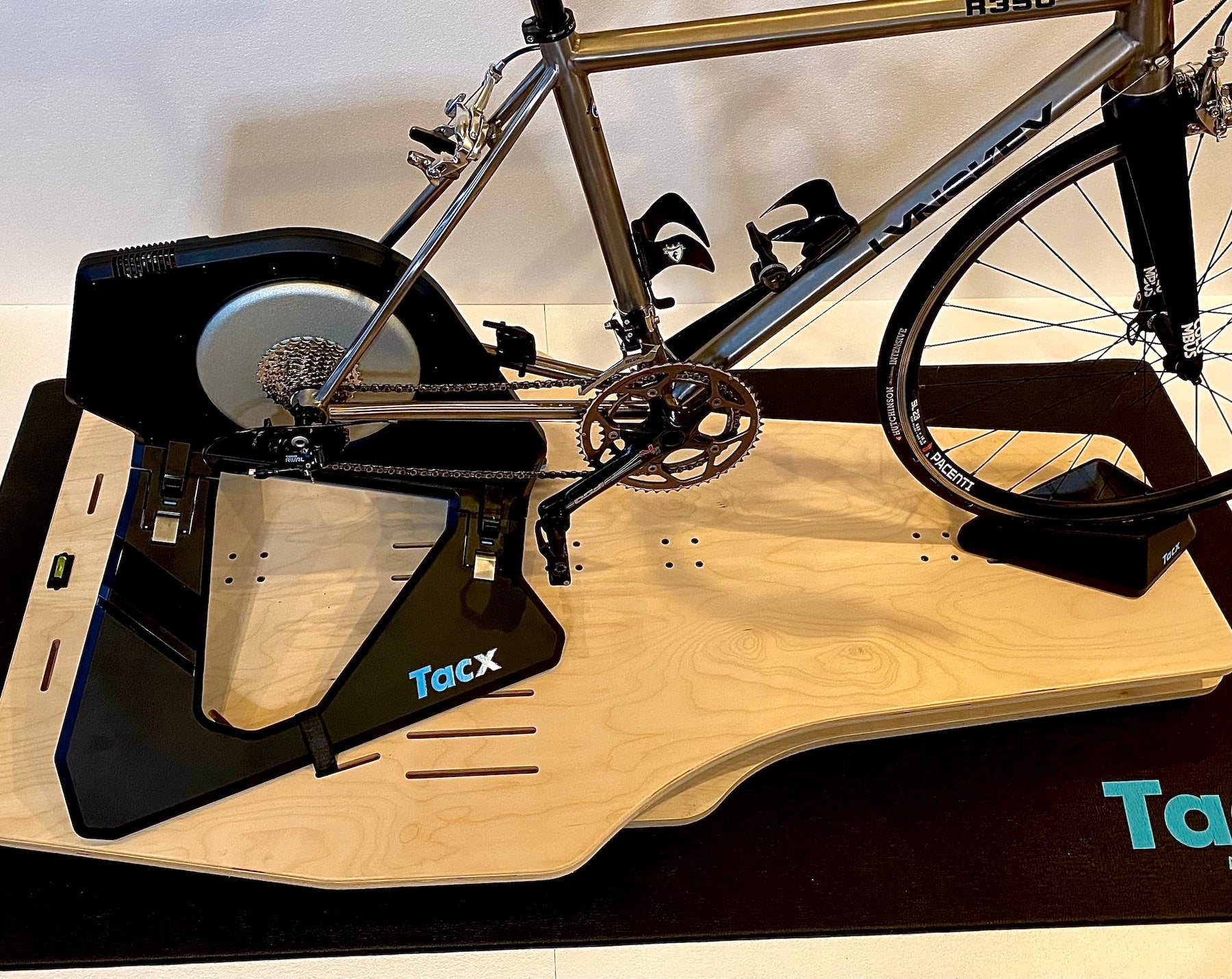 An unpainted Velocity Rocker rocker plate with a Lynskey titanium bike and Tacx Neo 2T smart trainer attached.